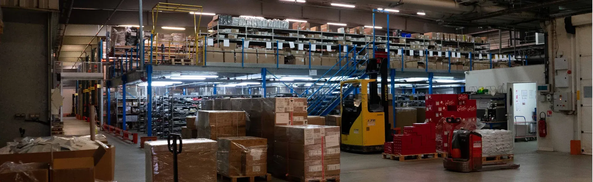 Vue large d'un entrepot logistique avec un transpalette et des colis/Wide view of a logistics warehouse with a pallet truck and parcels